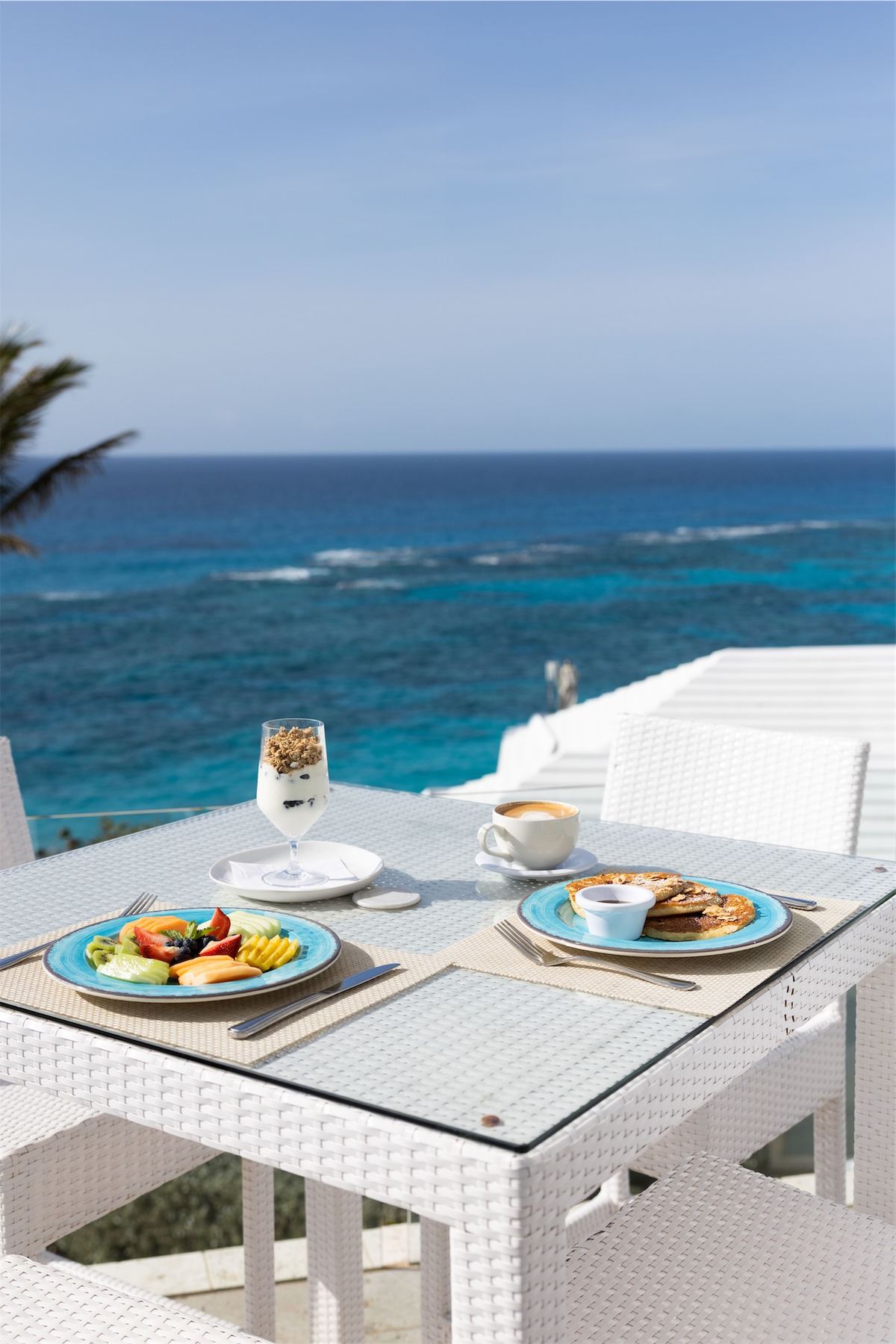 Breakfast for two set on a white terrace table high above the reef