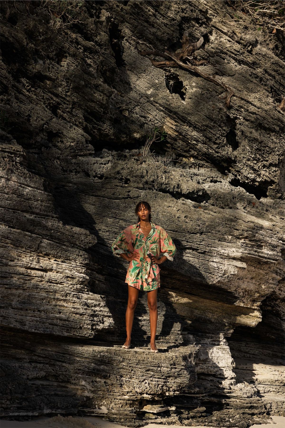 Model in a printed resort set standing in the shadow of a dark rock formation