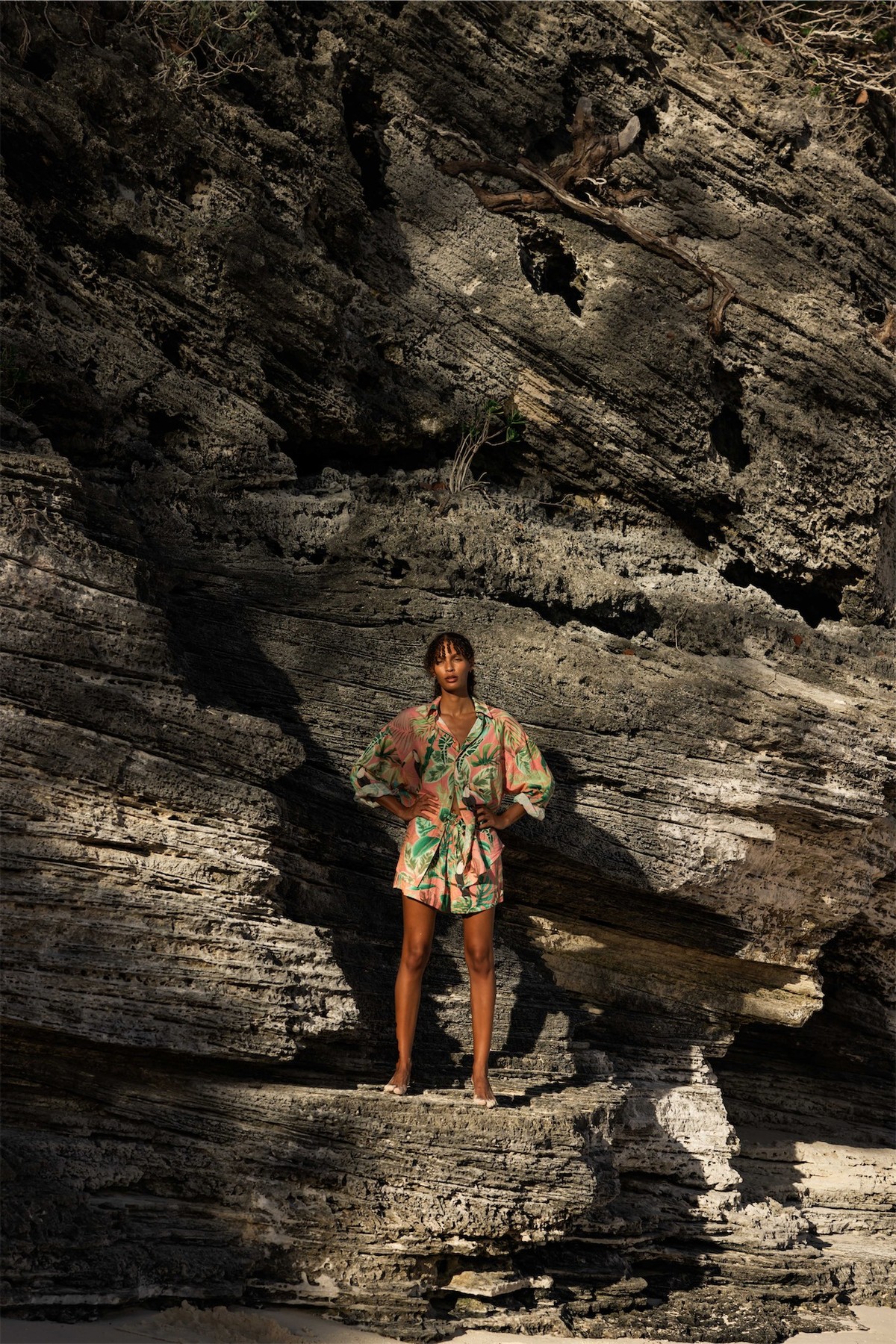 Model in a printed resort set standing in the shadow of a dark rock formation