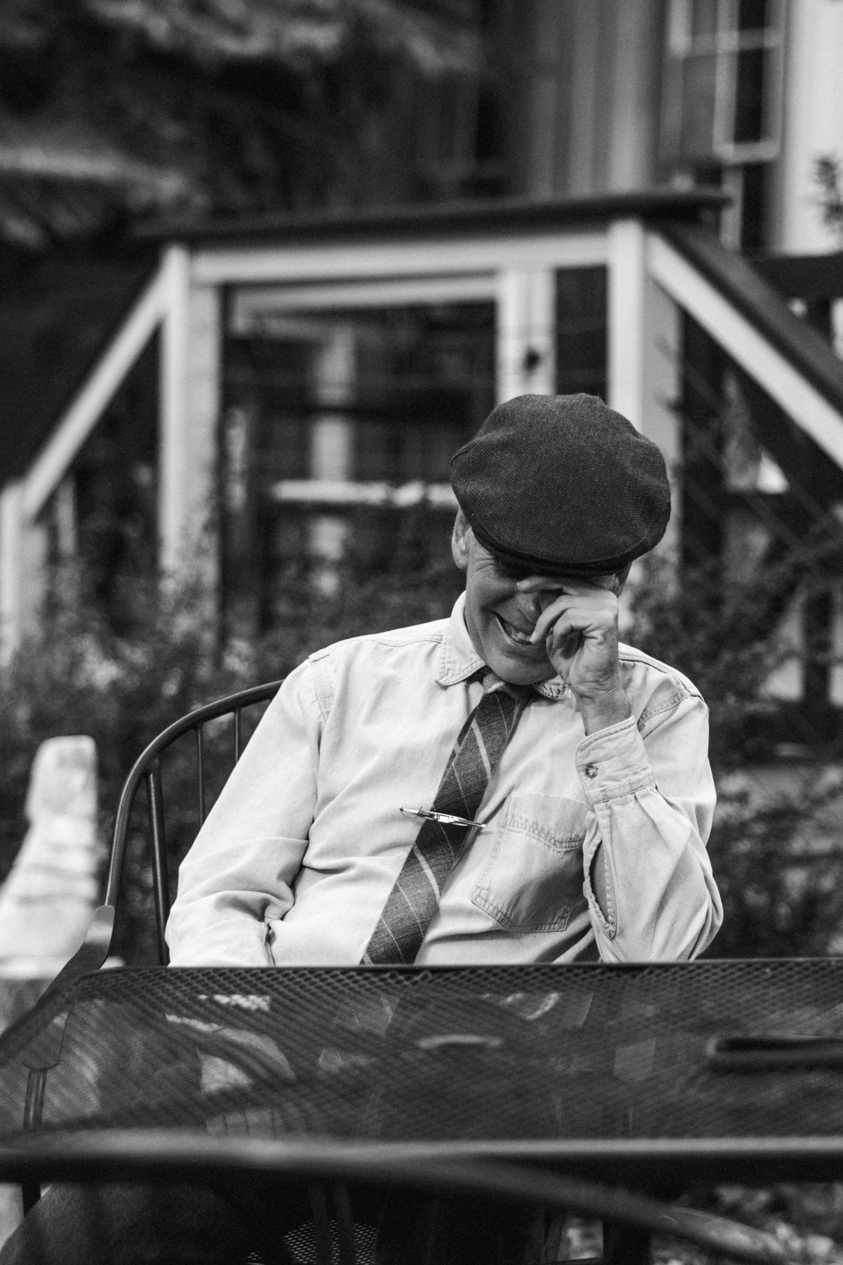 A guest in a flat cap wipes away a tear at the welcome dinner at a mountain ranch among the aspens, black and white