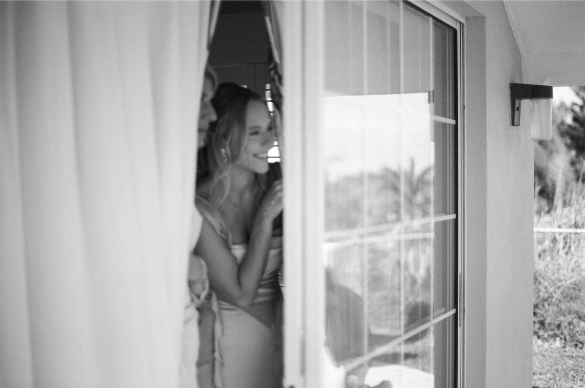 Black and white glimpse of the bride through a doorway behind sheer curtains
