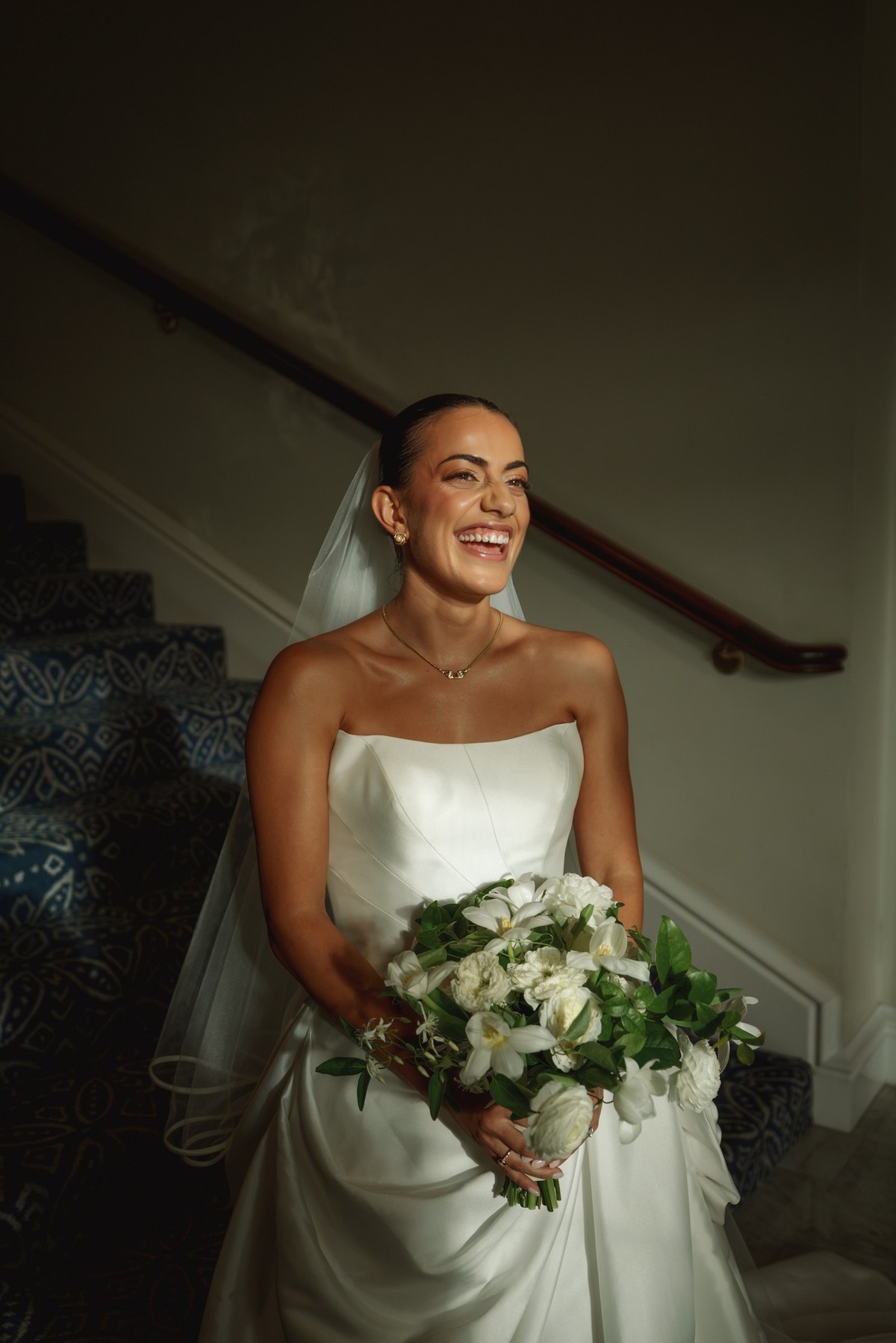 Bride laughing on the staircase holding a white bouquet at Rosewood Bermuda