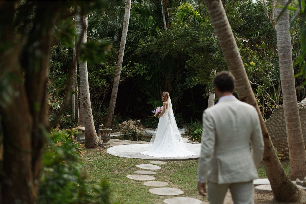 Groom waiting on a stepping stone path as his bride approaches through the palms