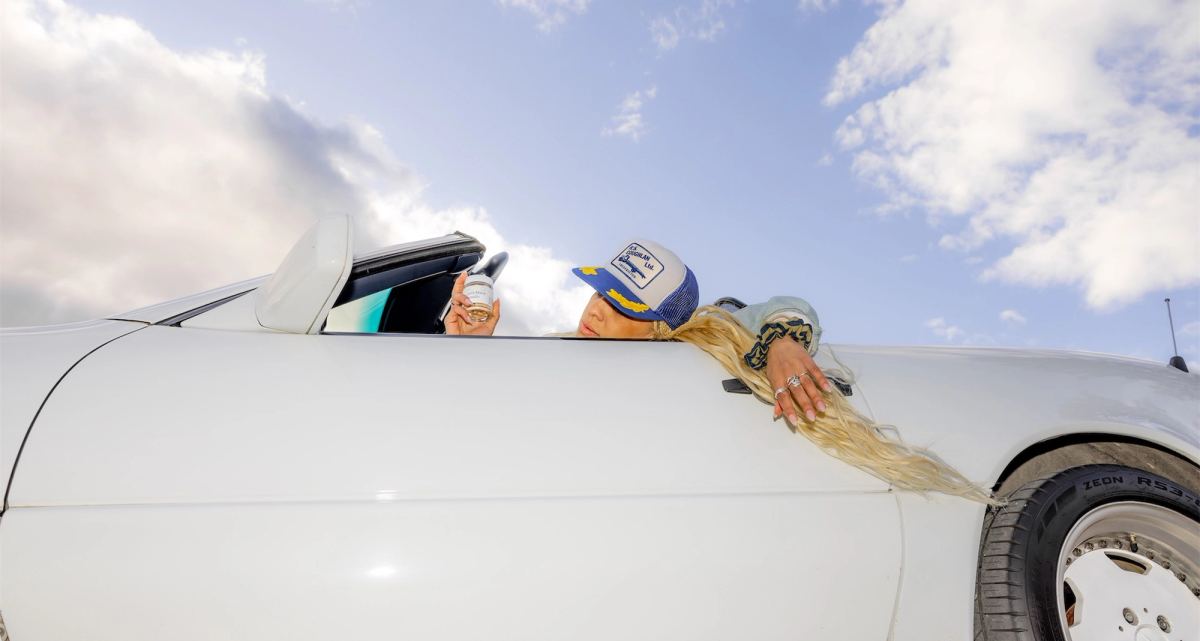 Passengers leaning out of a white convertible, hair flying against the sky