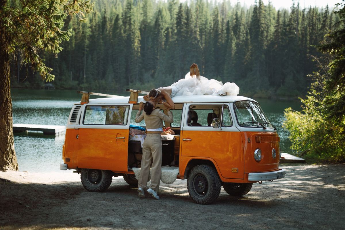 Orange VW camper van parked by the lake as the couple stand alongside it
