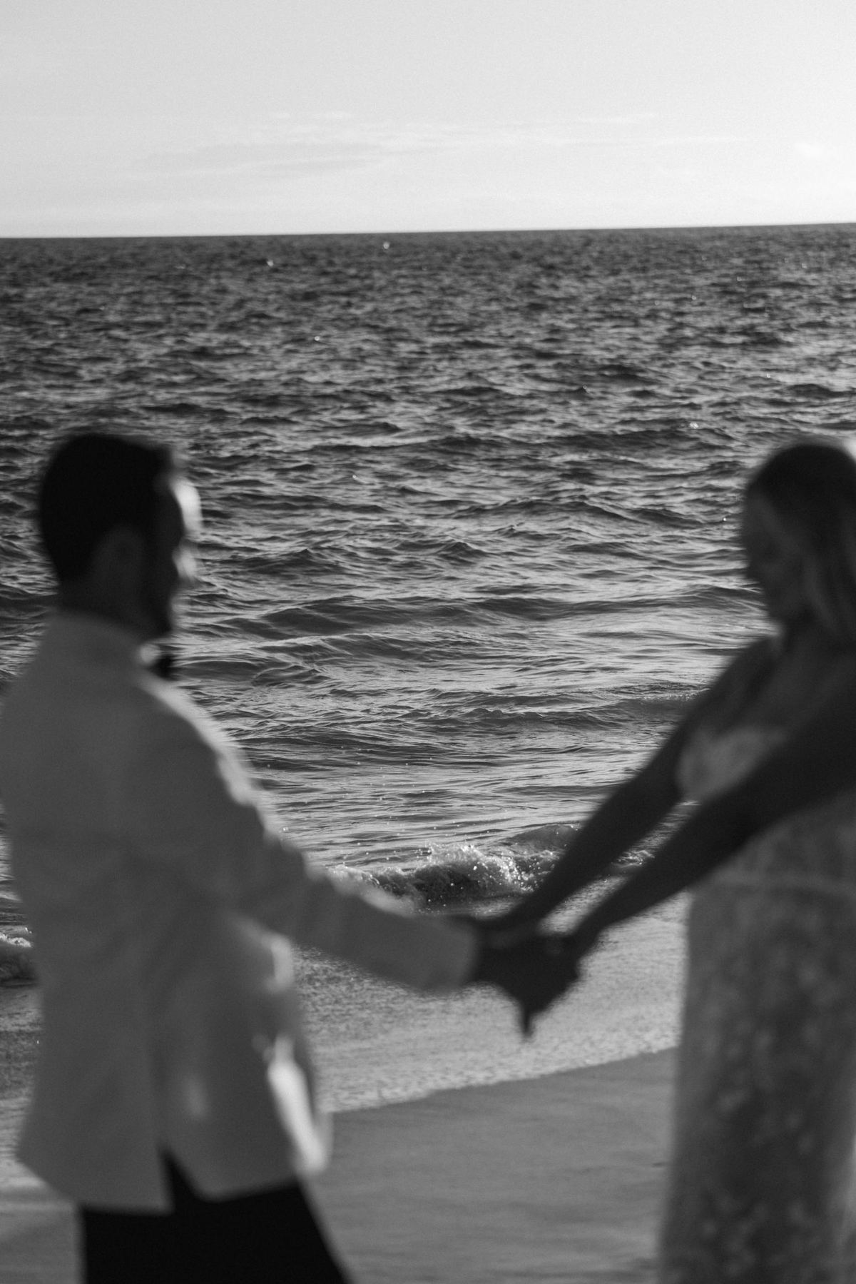 Black and white silhouette of couple holding hands at ocean during Bermuda wedding