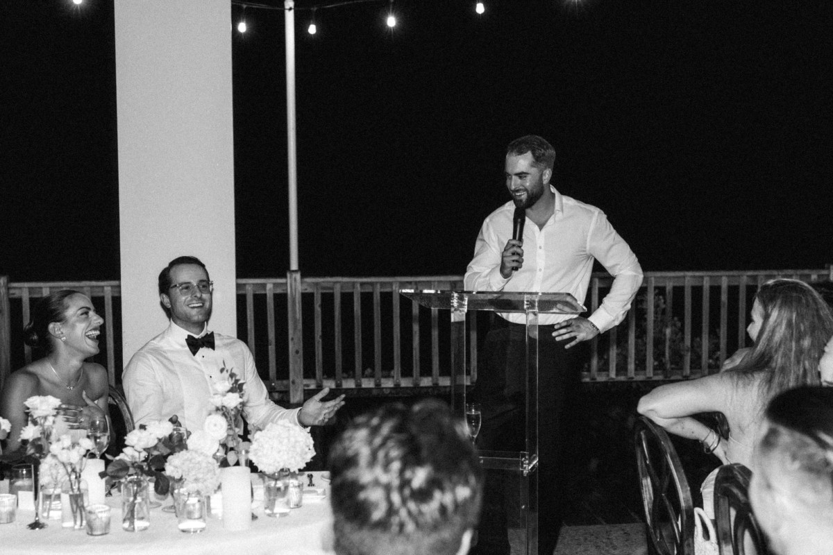 Groomsman giving a toast as the couple laughs at their table at Rosewood Bermuda