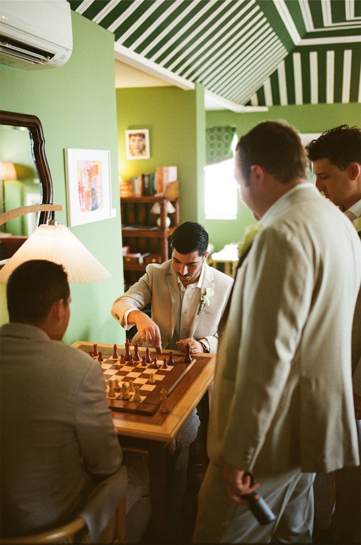 Groomsmen gathered over a backgammon board in a green walled sitting room