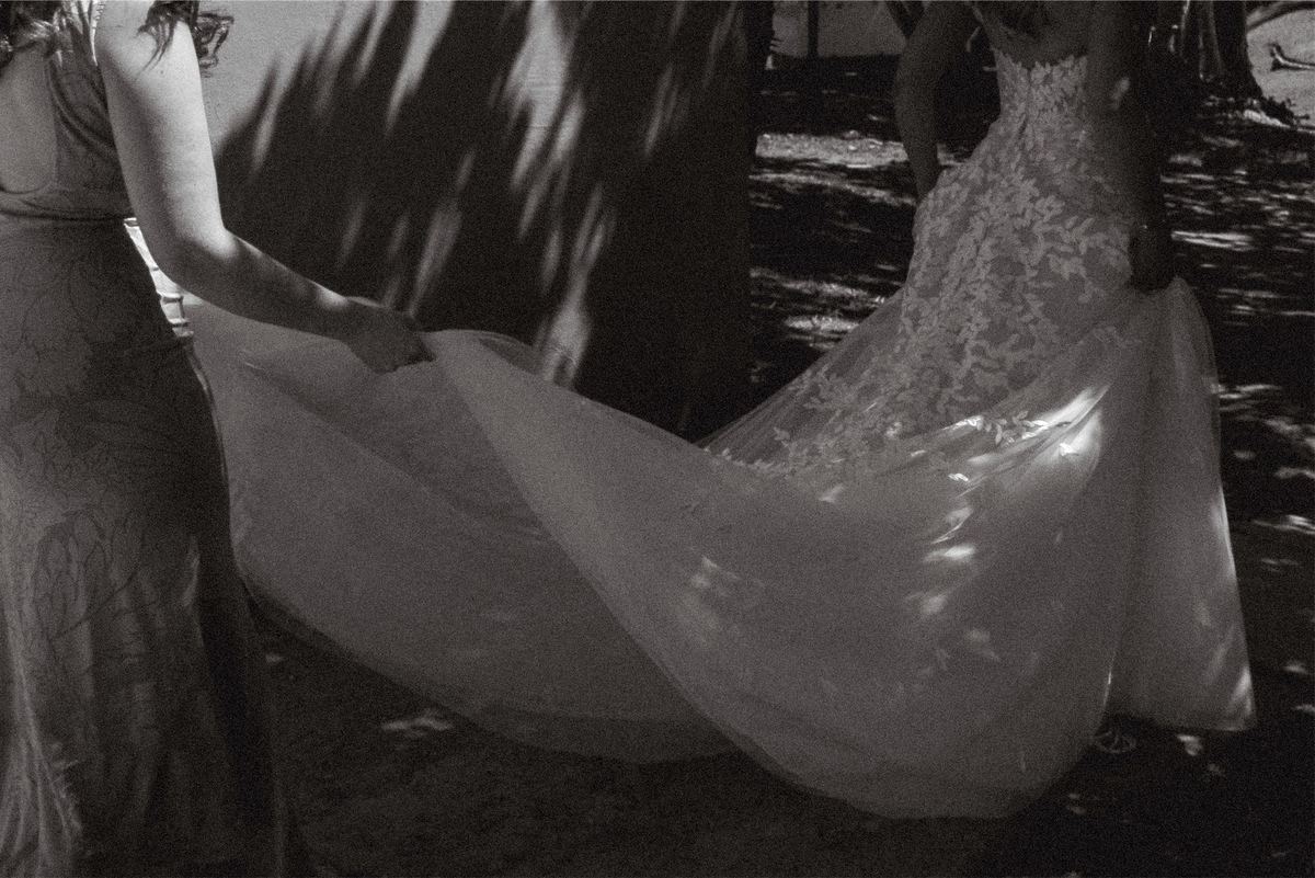 Black and white detail of the bride's lace train being carried across the lawn