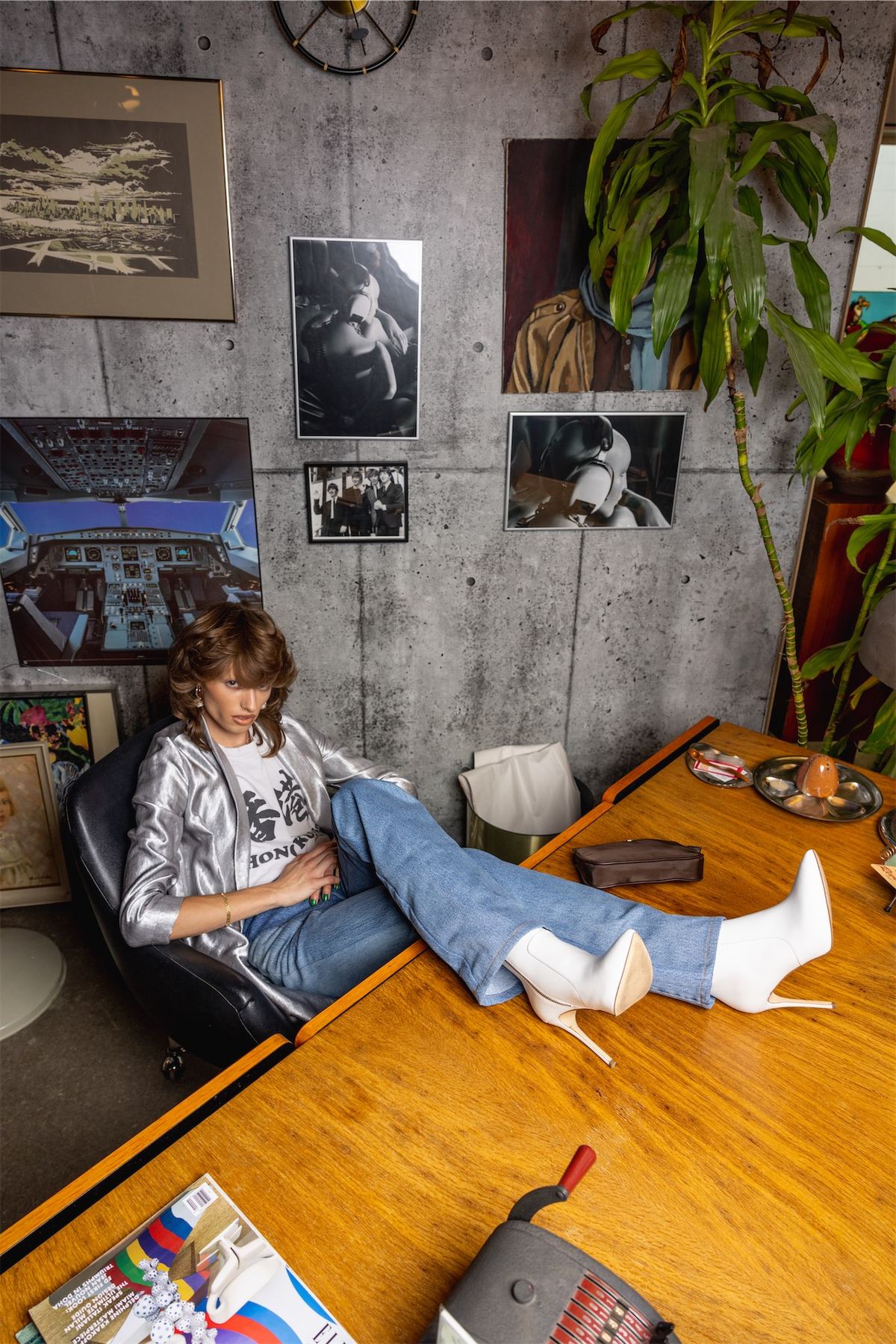 Model in a printed top stretched across a wooden table in a plant-filled room