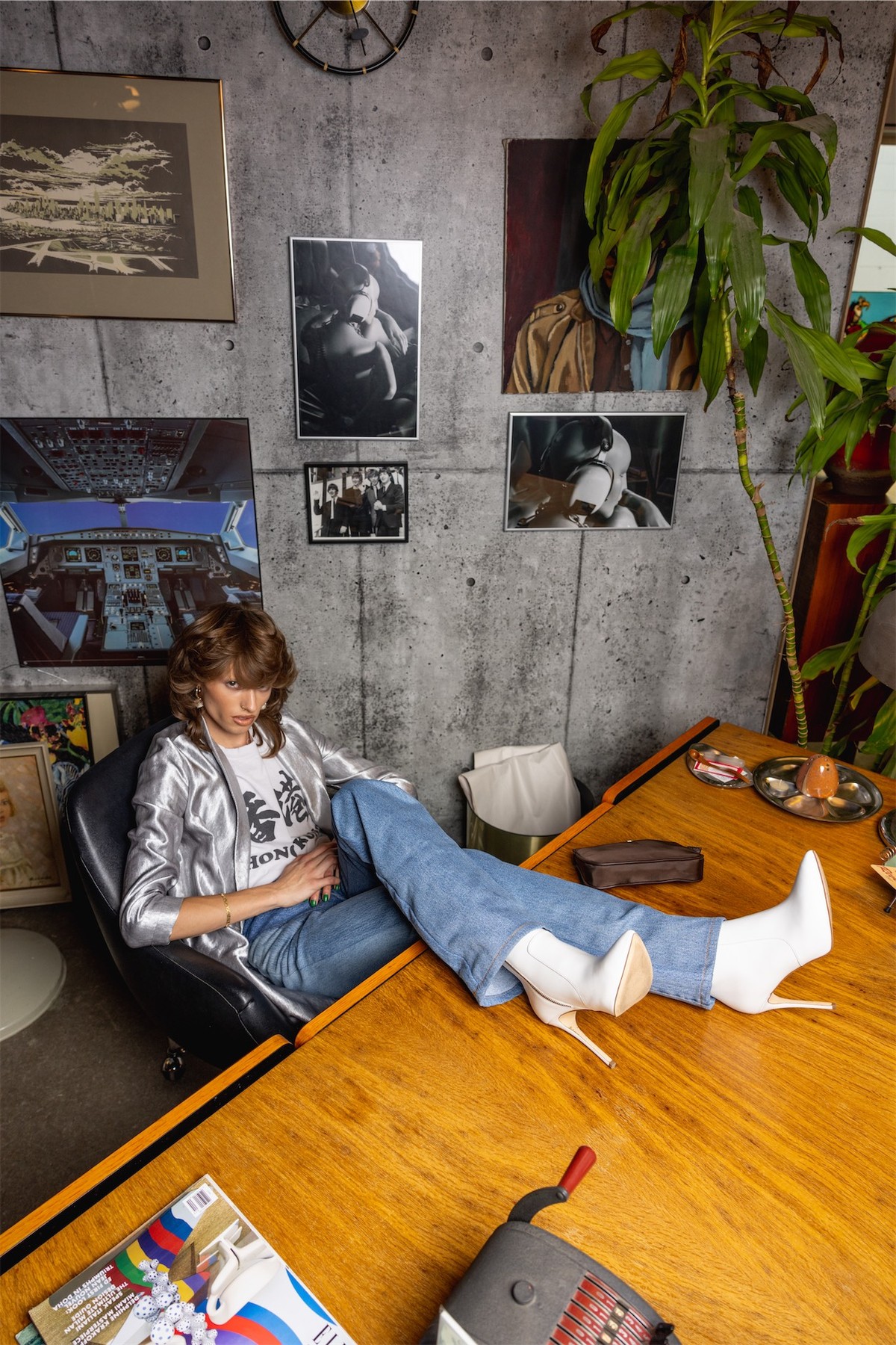 Model in a printed top stretched across a wooden table in a plant-filled room