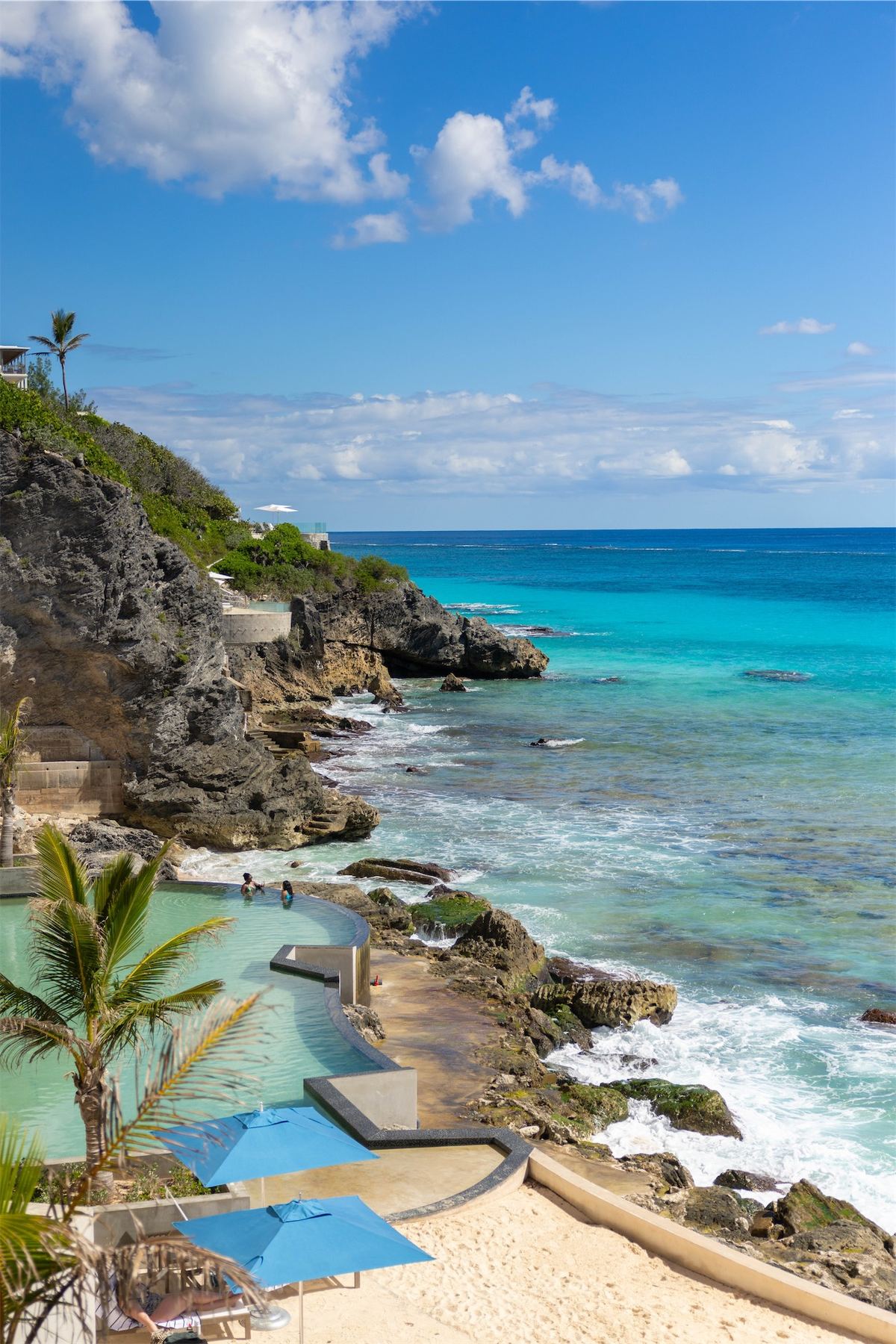 Cliffside resort pool terrace looking out over a turquoise cove and rocky shoreline