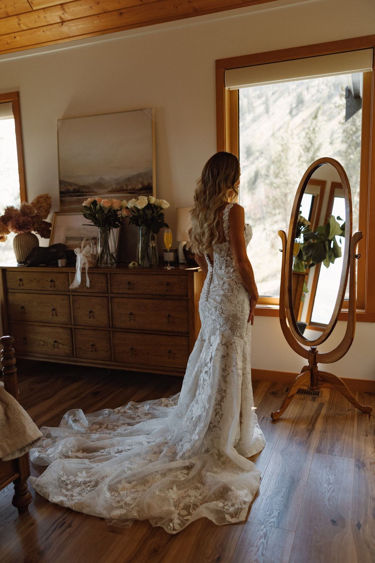 Bride alone in the room beside a standing mirror in her lace gown