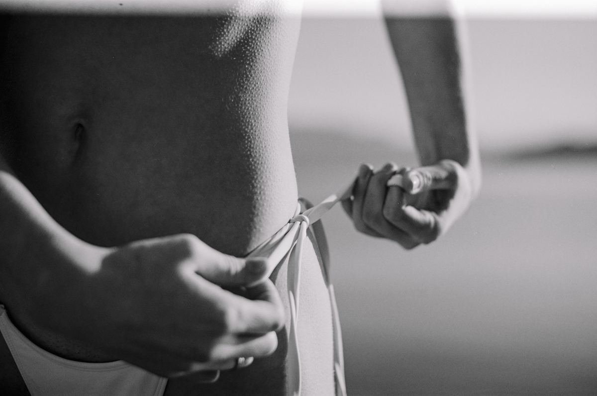 Black and white close-up of hands tying the side strings of a bikini bottom