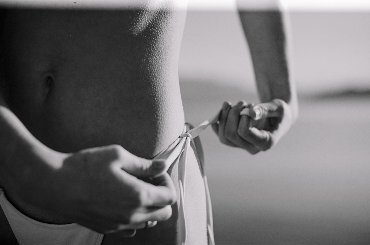 Black and white close-up of hands tying the side strings of a bikini bottom