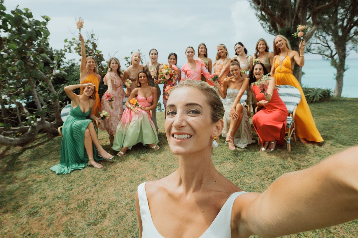 Bride taking a selfie with her bridesmaids in colourful gowns on the lawn