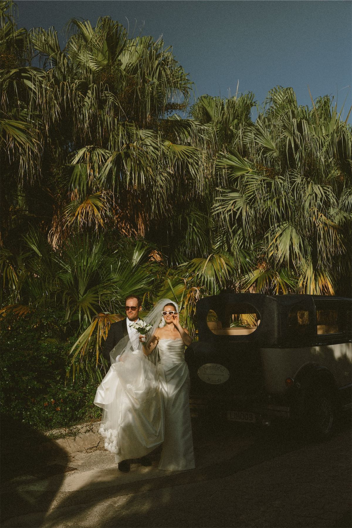 Bride and groom beside a vintage car under a wall of palms