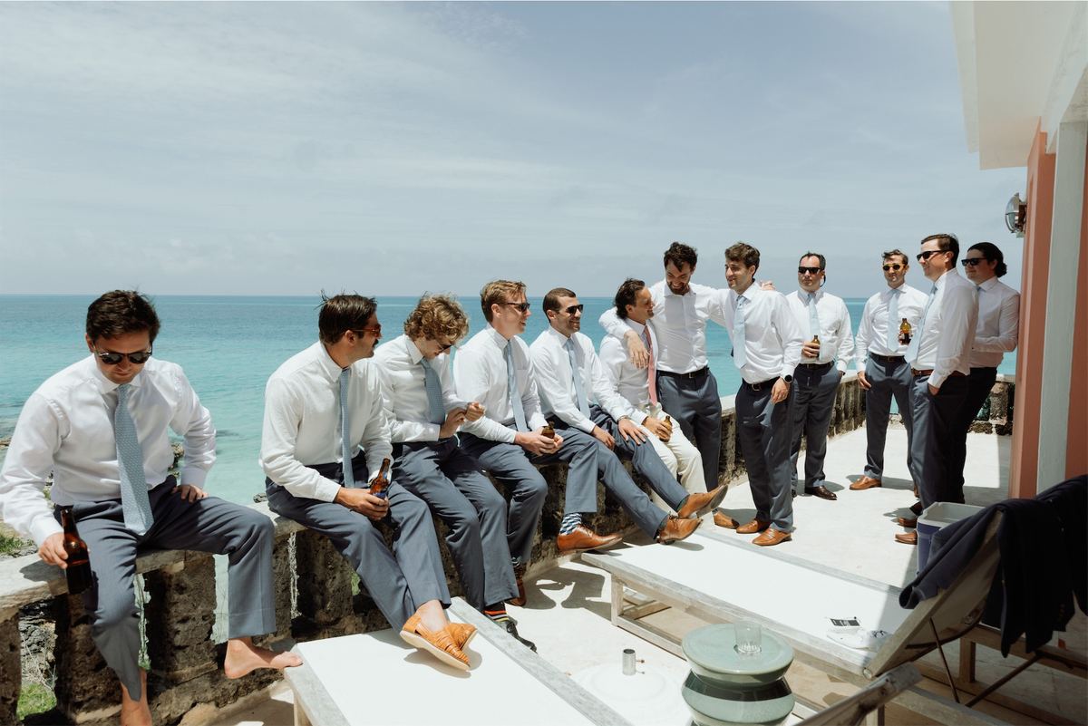 Groomsmen with sleeves rolled up lounging on a terrace above the water