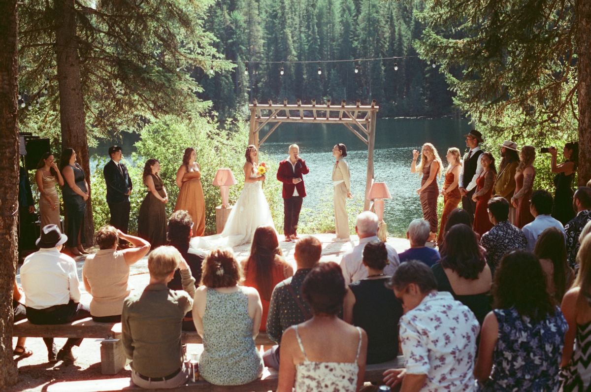 Lakeside ceremony seen over the guests, the wedding party under a timber arch