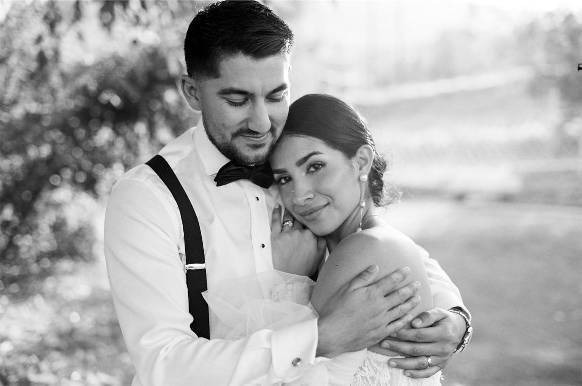 Black and white close portrait of the groom holding his bride from behind