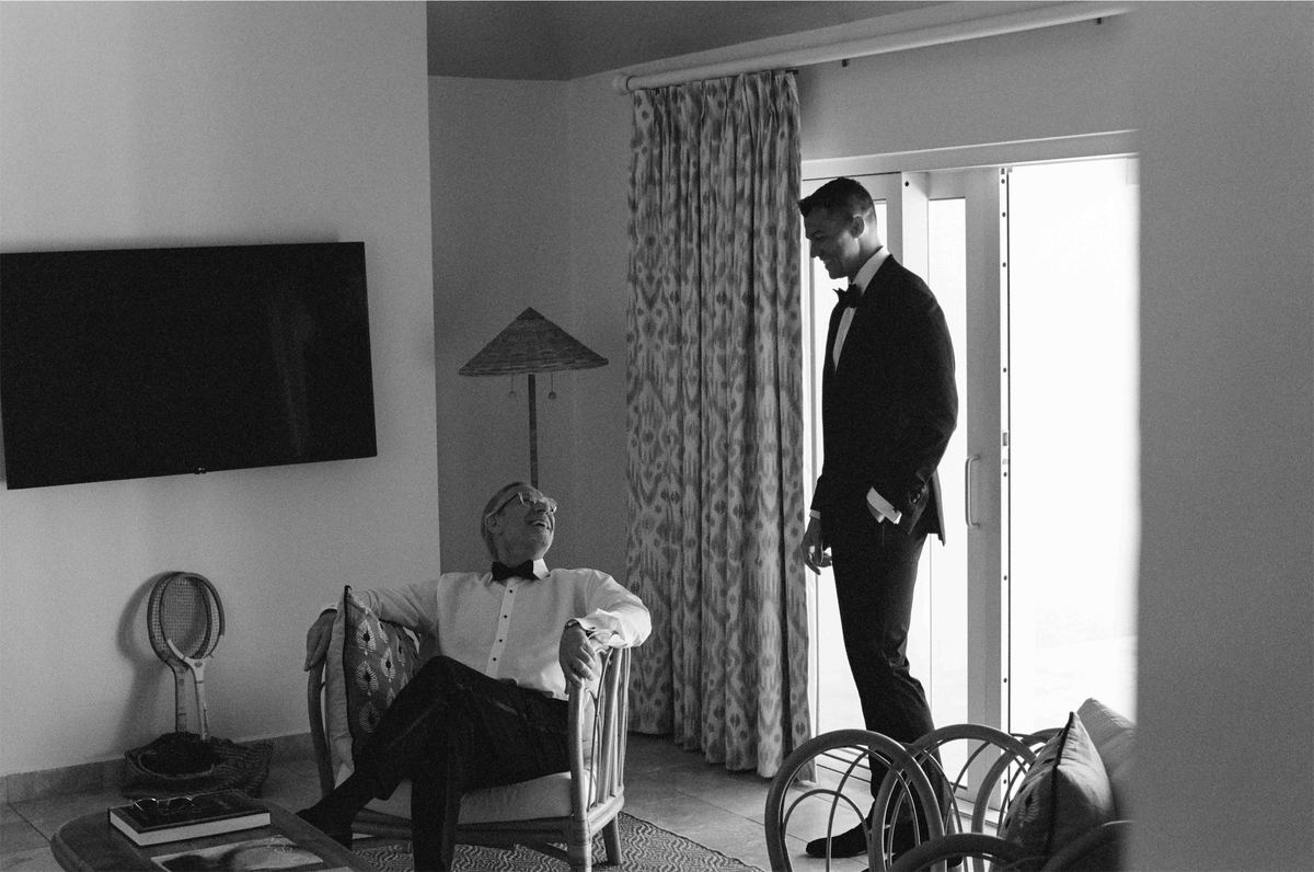Black and white of the groomsmen getting ready in a suite, one waiting at the window