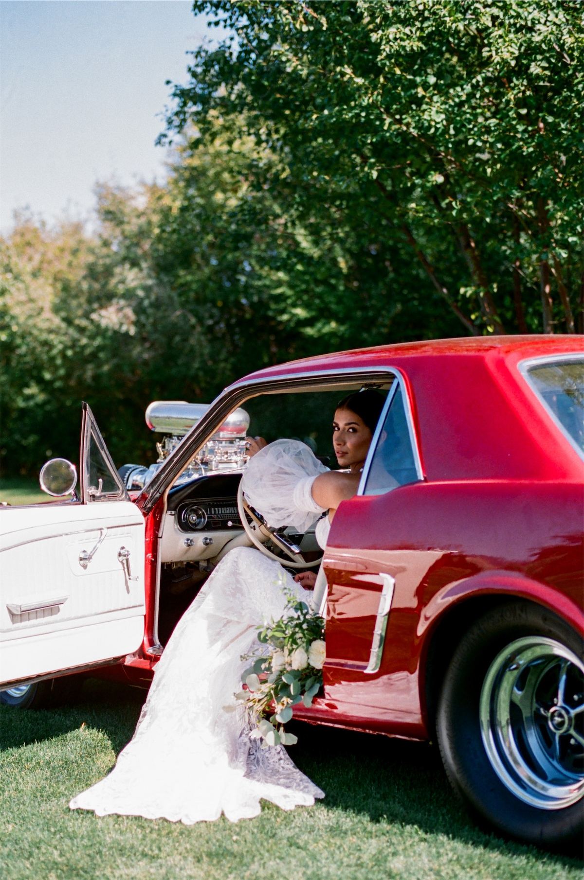 Bride stepping out of a red vintage Mustang parked on the lawn