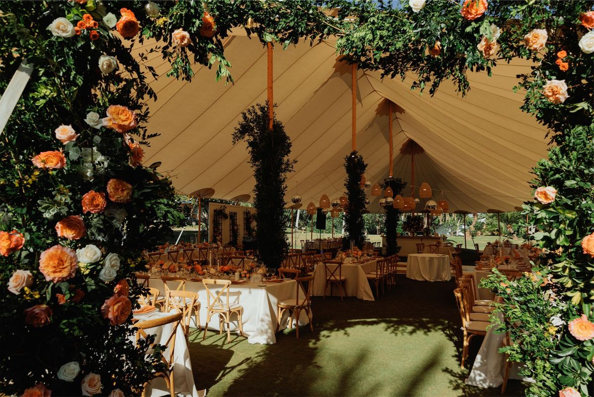 Tented reception seen through an arch of orange roses and trailing greenery