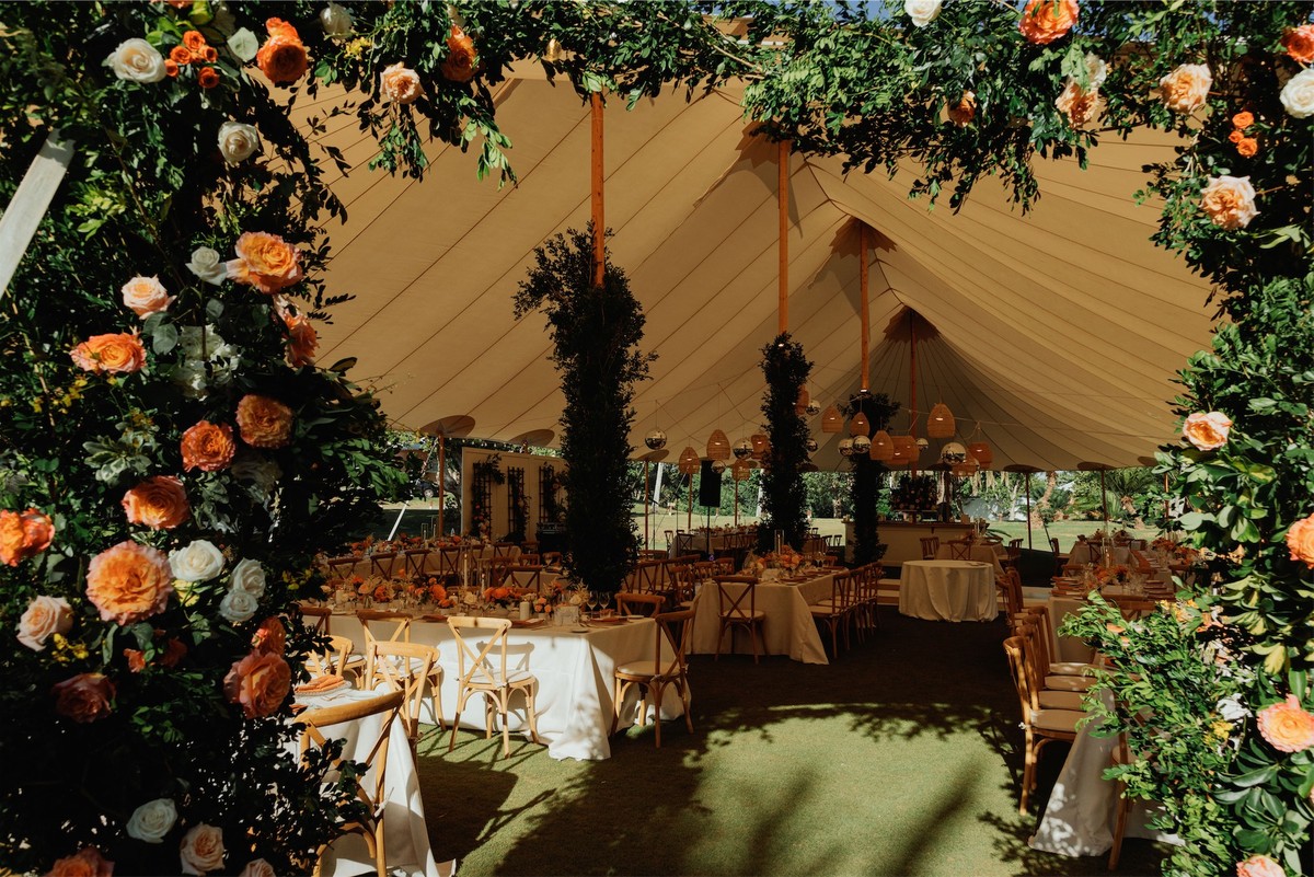 Tented reception seen through an arch of orange roses and trailing greenery
