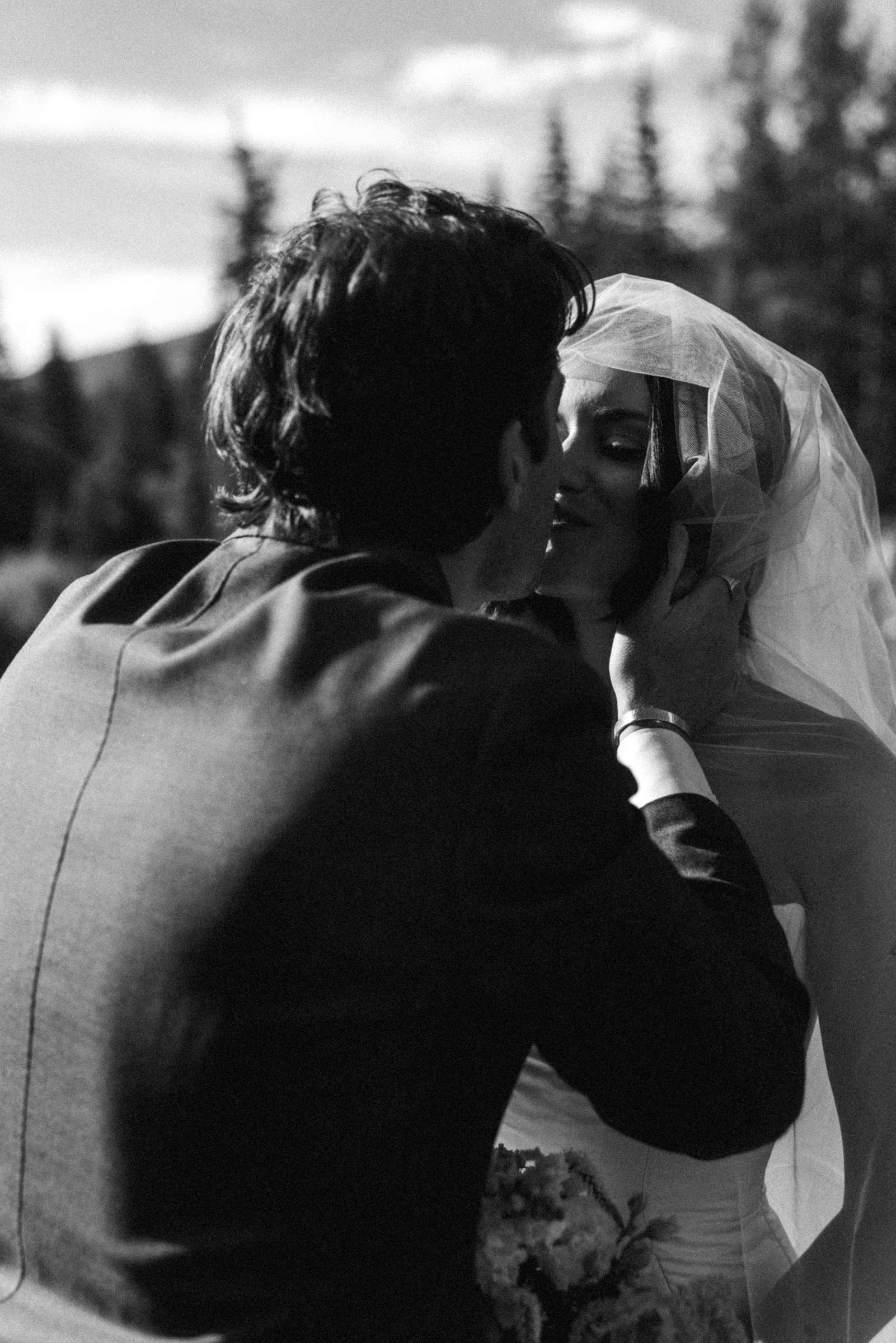 Owen kisses Devin in her veil at a mountain ranch among the aspens, black and white