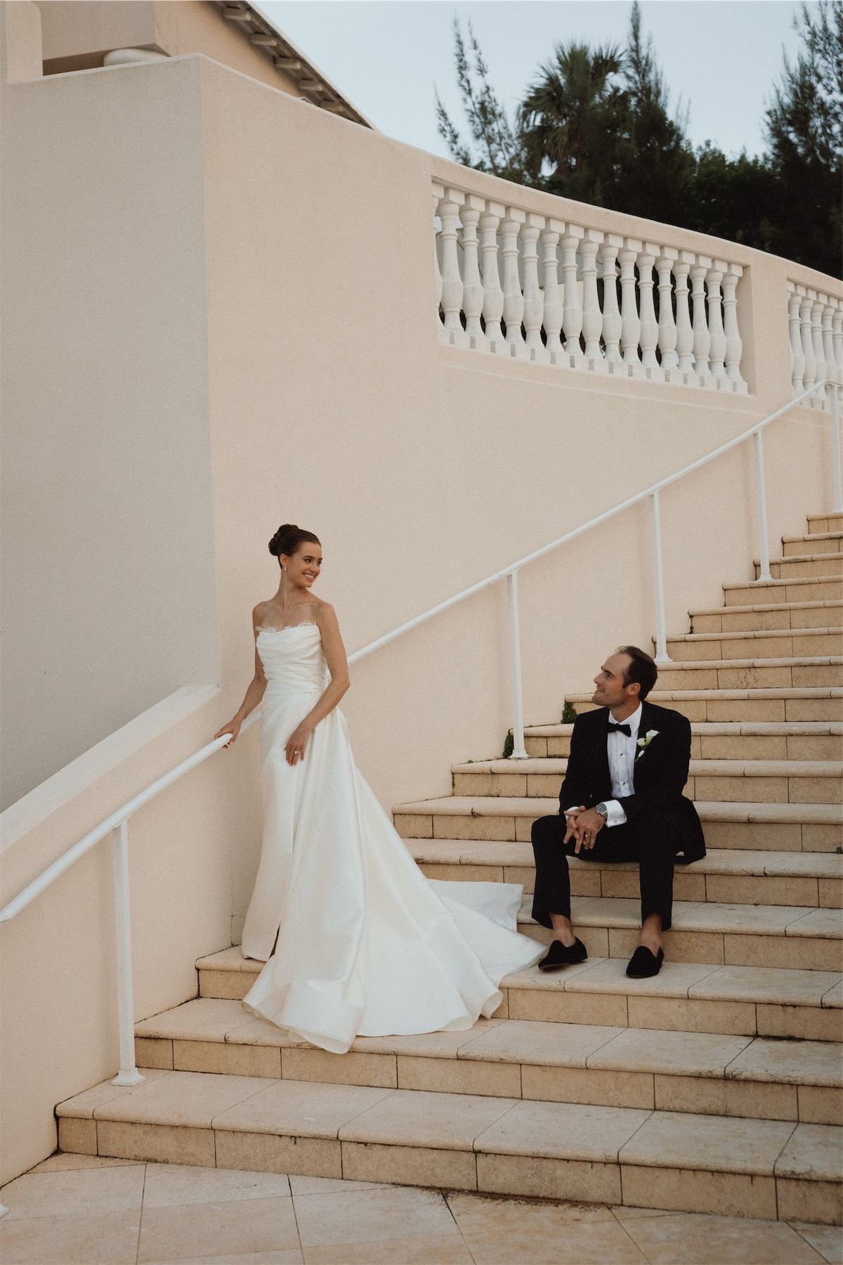 Bride on a pale staircase while the groom rests on the steps below