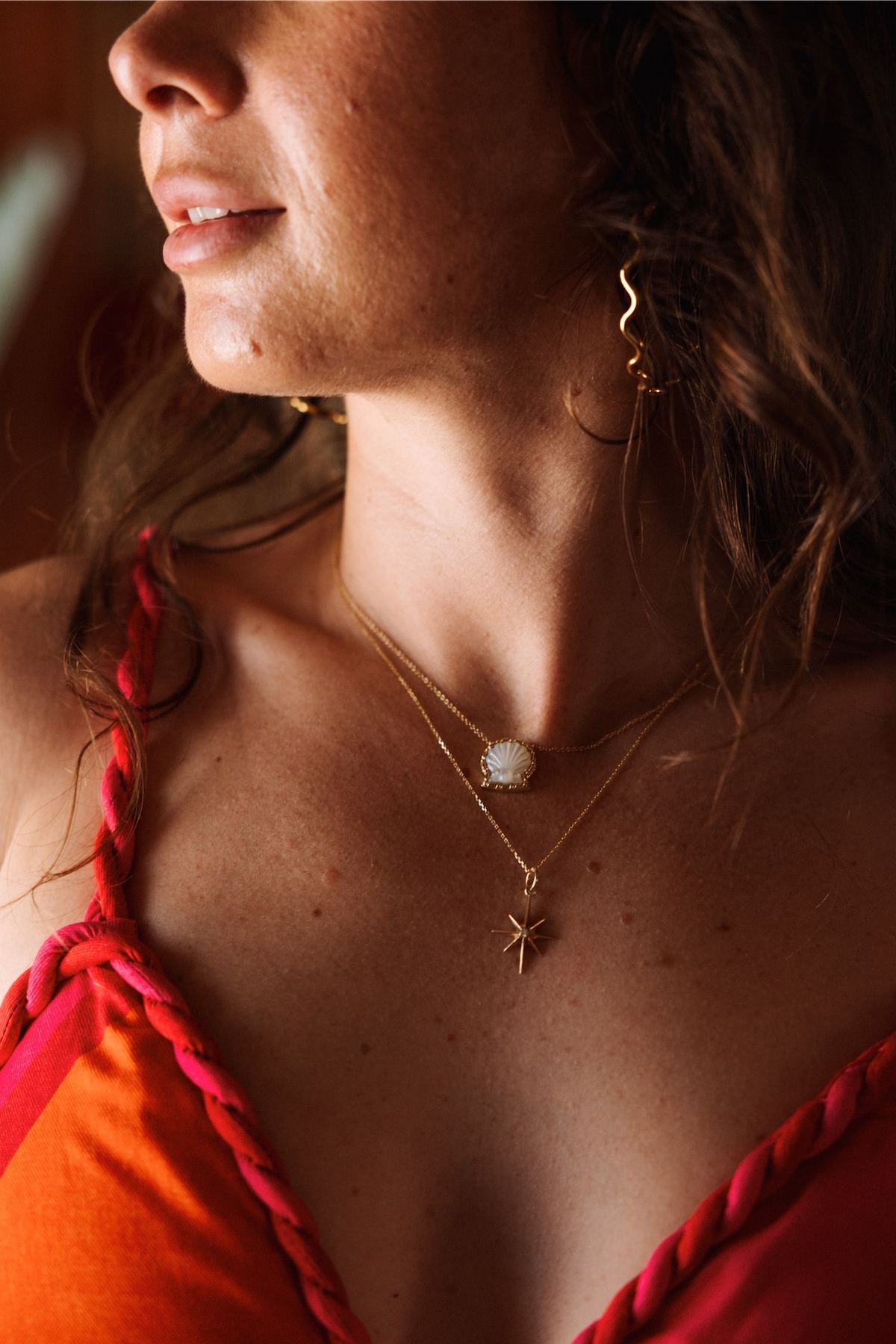 Detail of layered gold necklaces worn with a red swimsuit in warm light