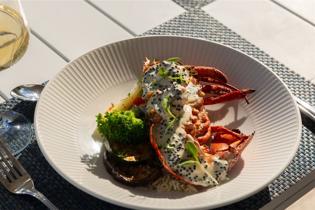 Plated lobster with black sesame and broccolini next to a glass of white wine