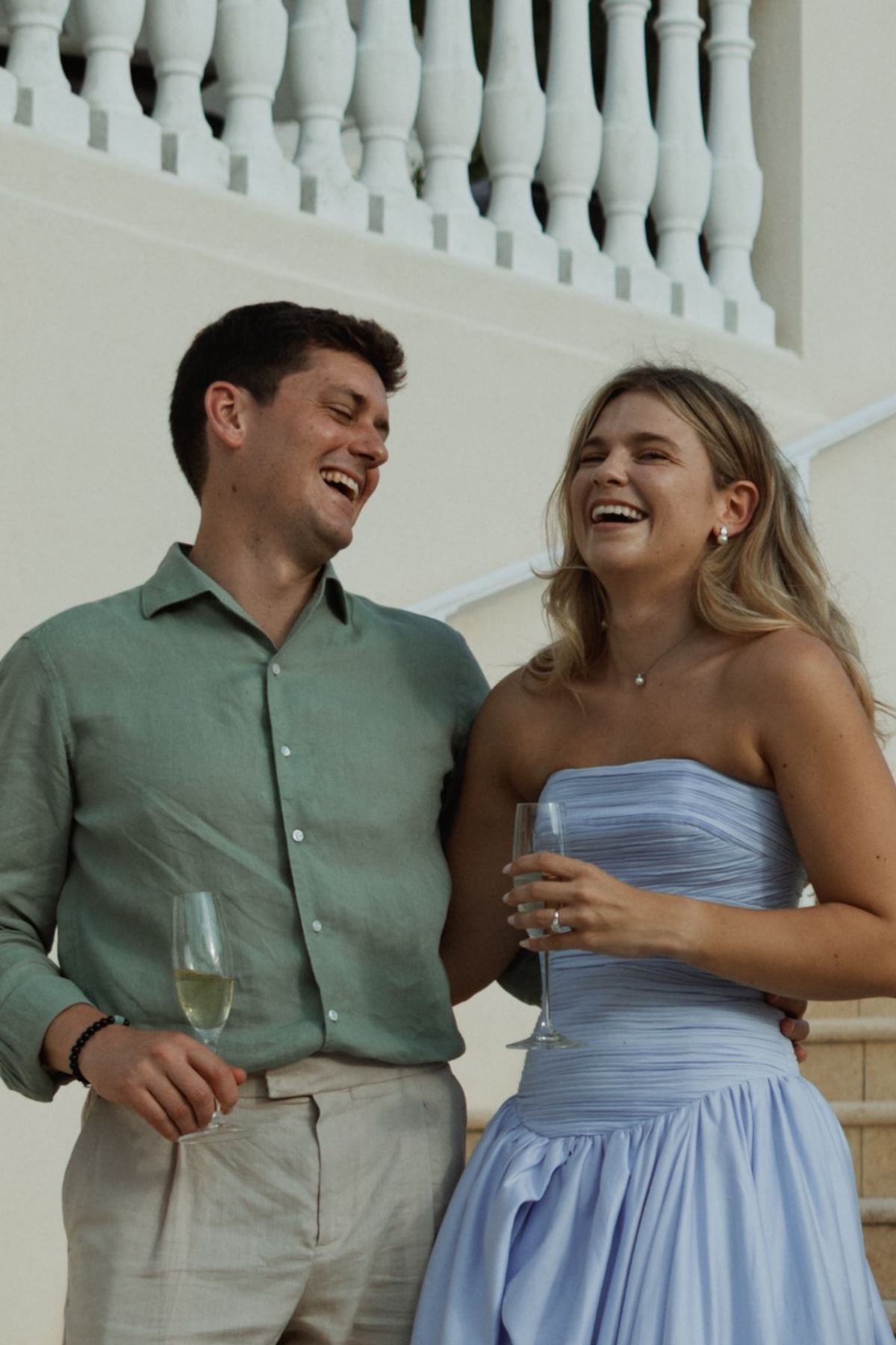 Two guests laughing together with drinks beside a white balustrade