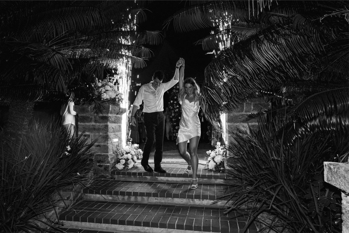 Black and white of the couple raising joined hands at the top of garden steps