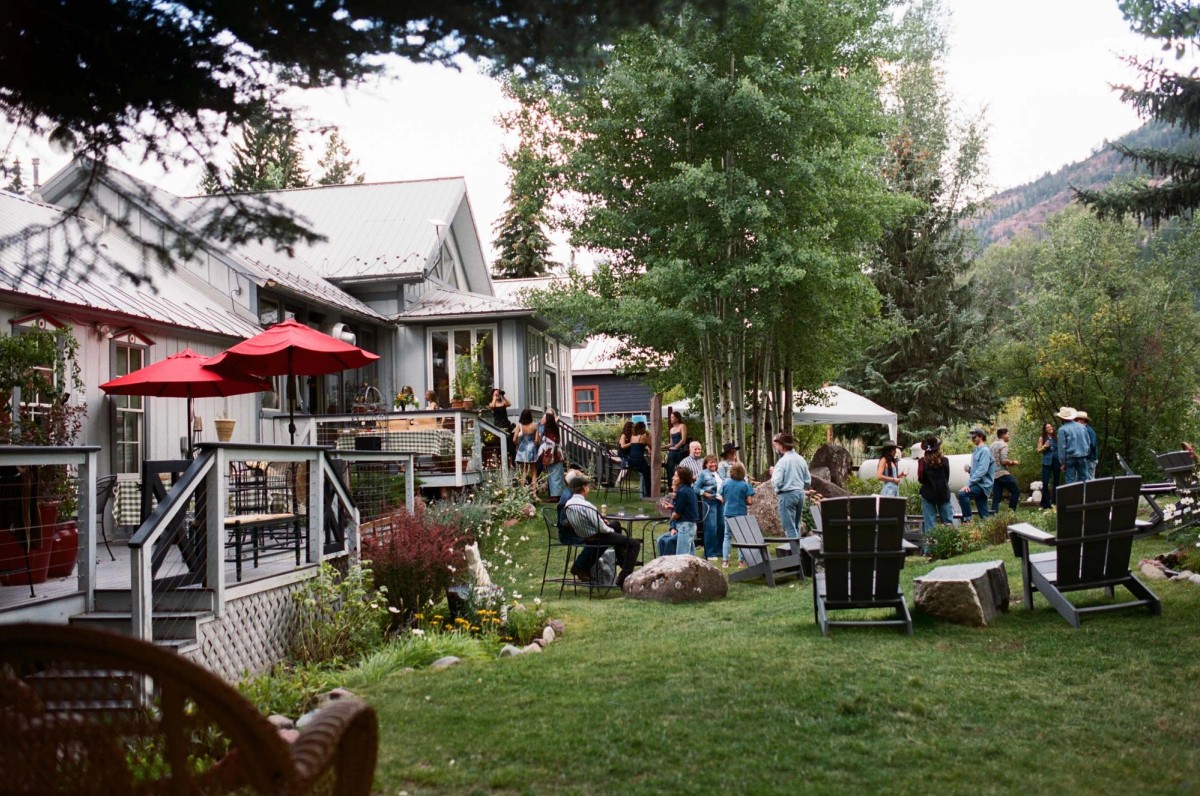 Guests gather on the lawn by the deck and red umbrellas, shot on film at a mountain ranch among the aspens