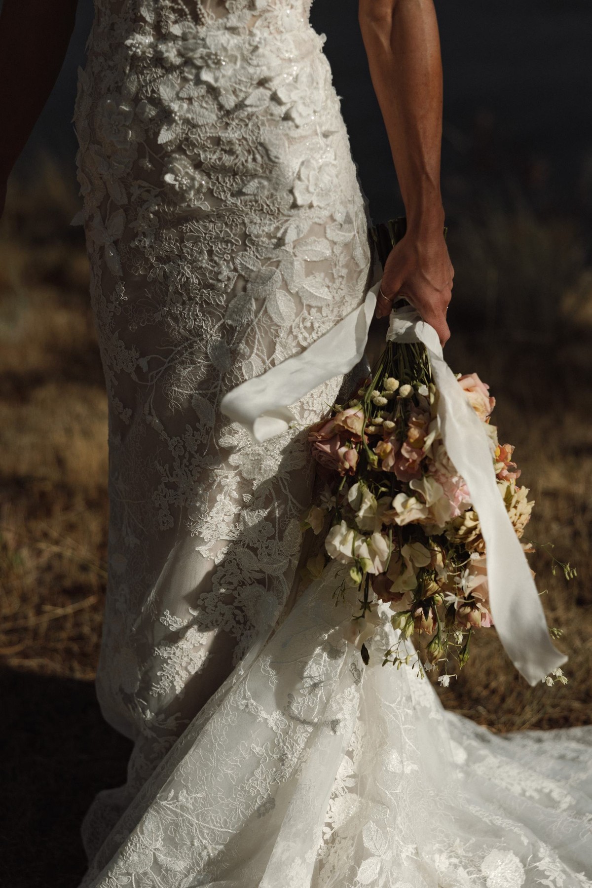 Bouquet held at the bride's side against the texture of her lace gown