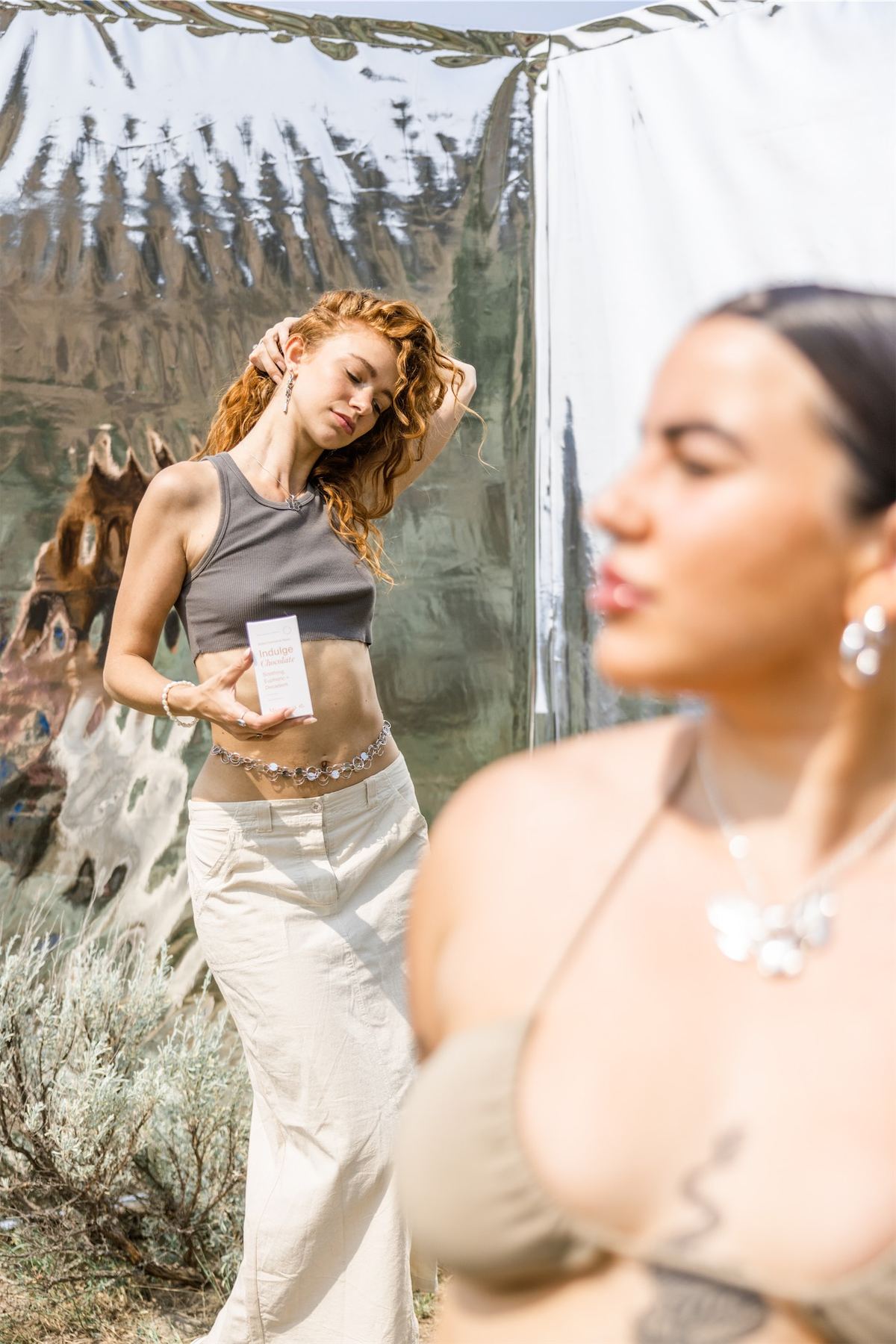 Two models with a capsule jar, one reflected in a mirror propped in the desert