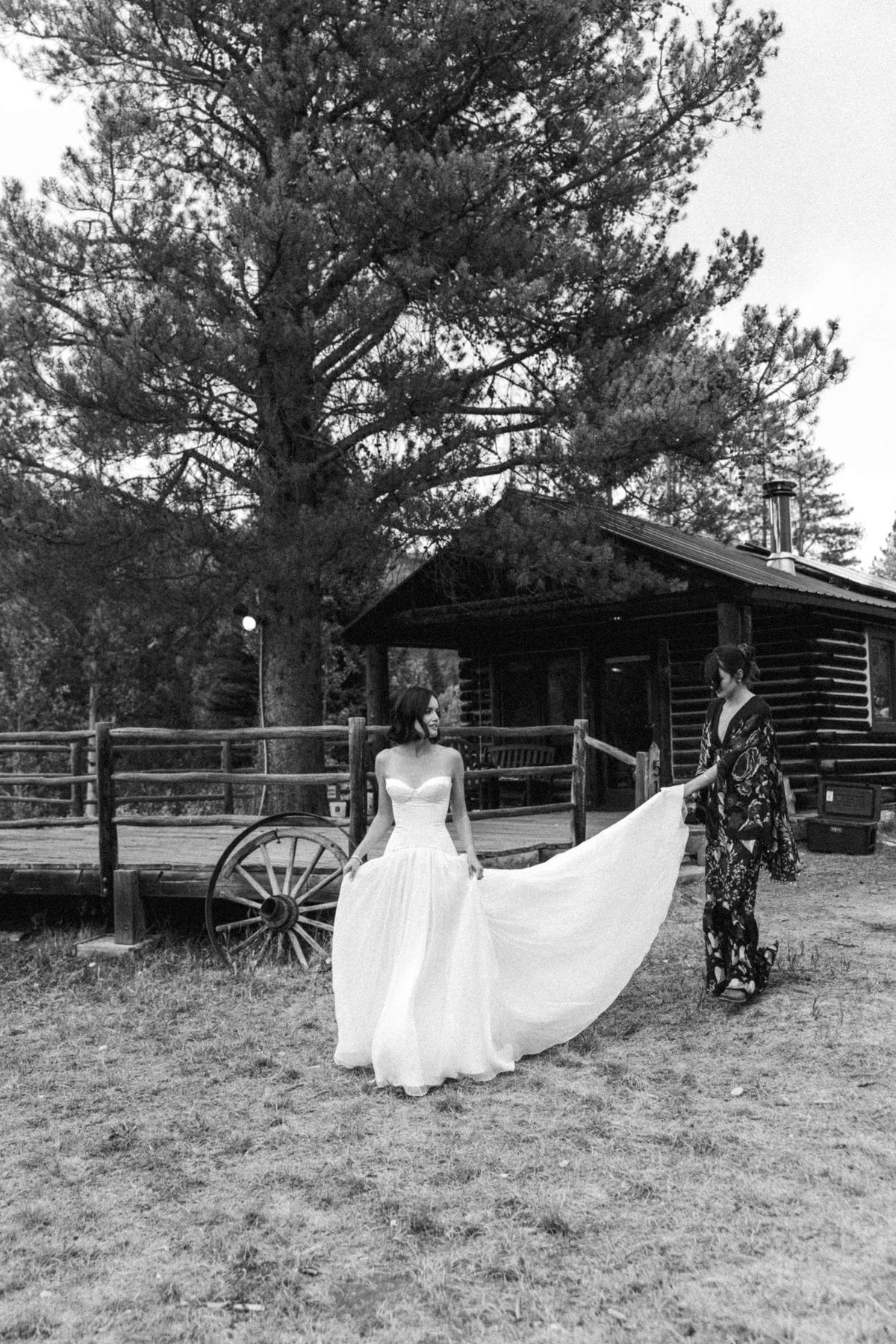 Devin's train is lifted as she walks past the old cabin at a mountain ranch among the aspens, black and white