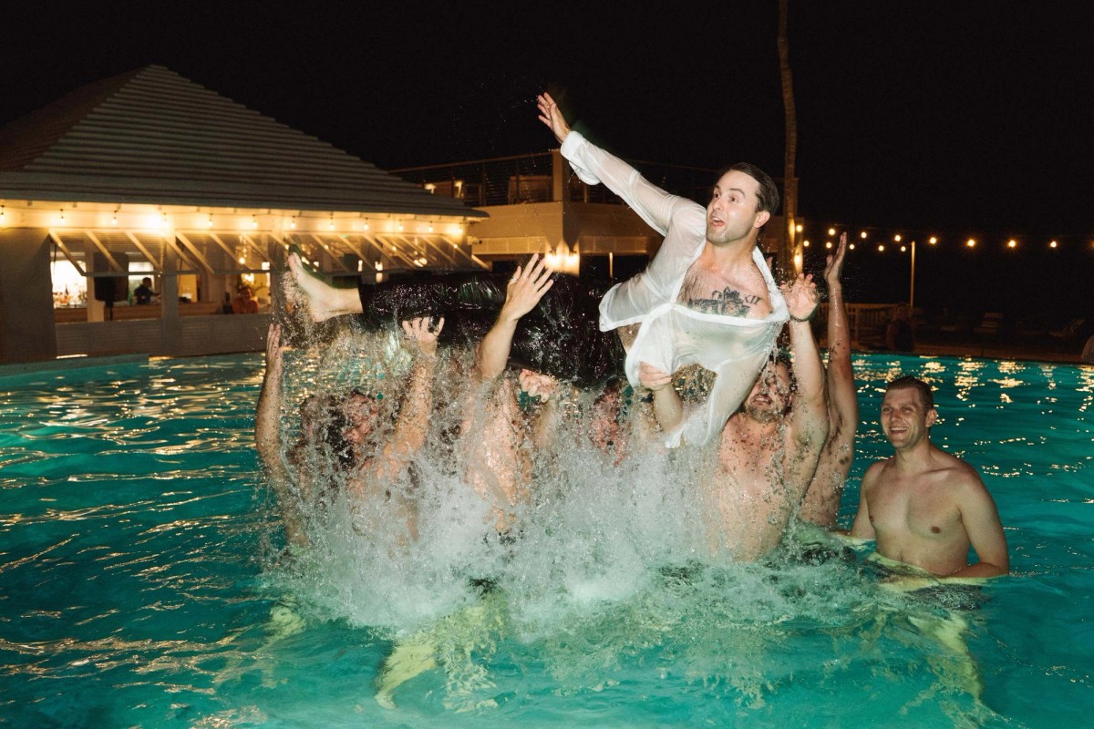 Groom lifted by his friends in the turquoise pool at night at Rosewood Bermuda