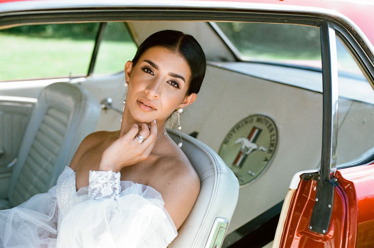 Bride posing in the front seat of a vintage red Mustang convertible