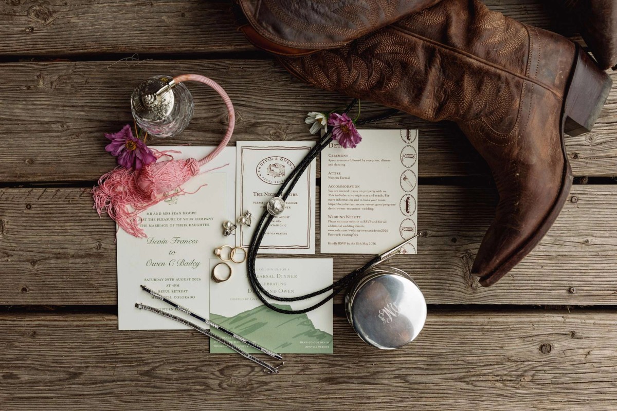 Cowboy boots, invitation suite, rings and bolo tie laid out on the cabin deck at a mountain ranch among the aspens