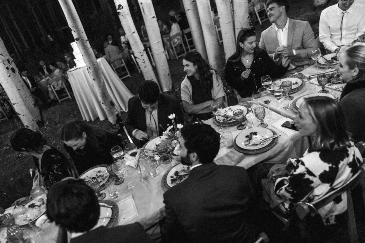 Guests laughing around the candlelit reception tables at a mountain ranch among the aspens, black and white