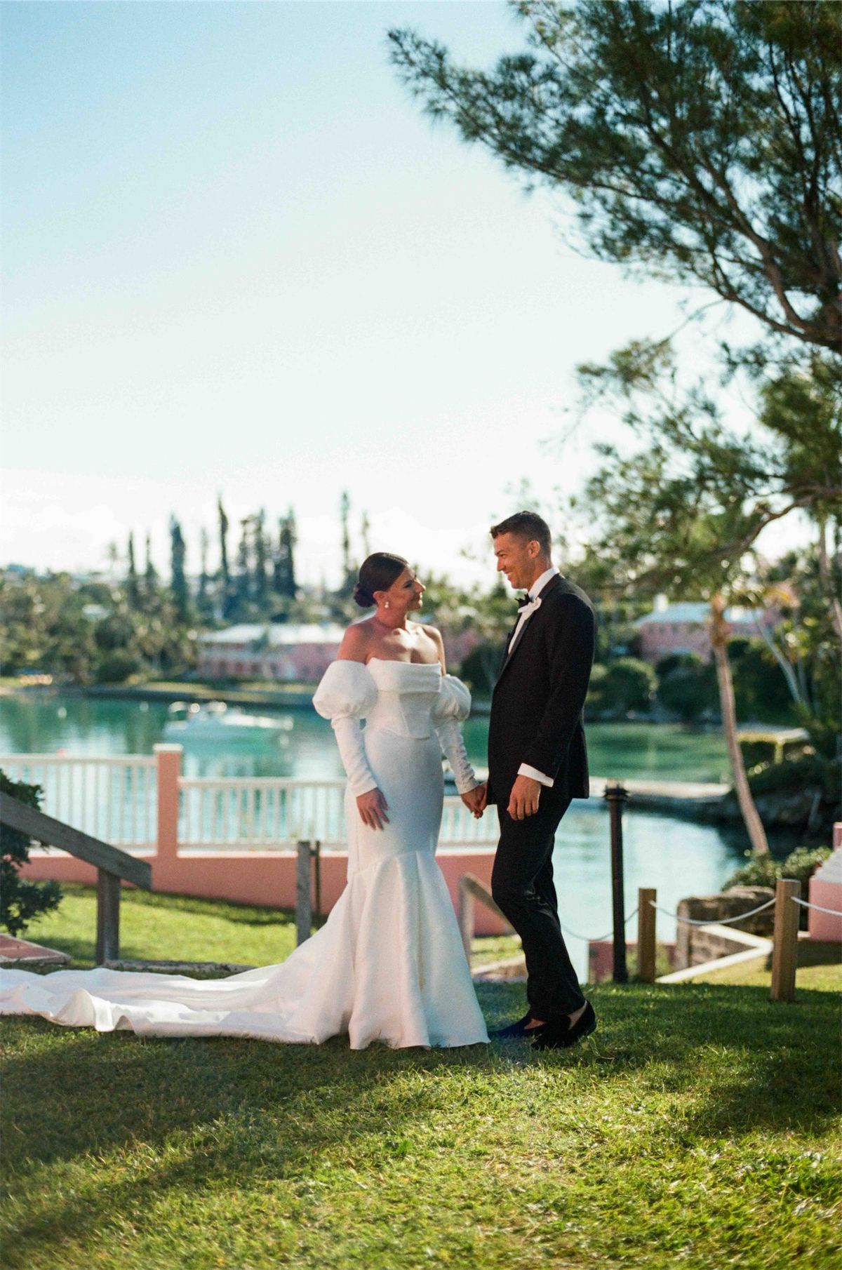 Bride and groom walking the lawn above the harbour in late afternoon light