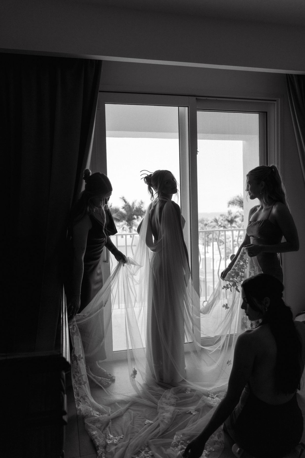 Bridesmaids getting ready by window, black and white documentary wedding photo