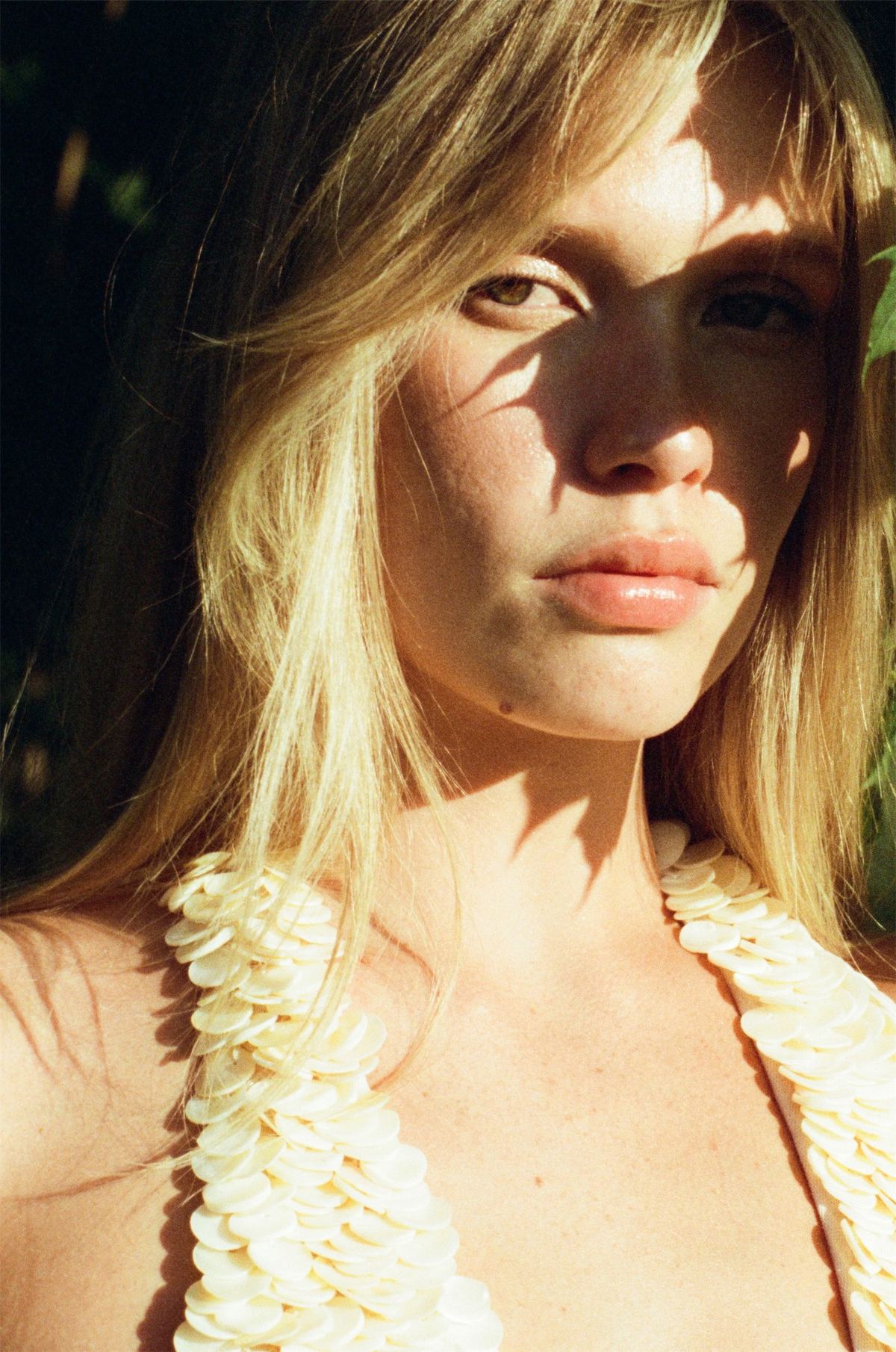 Sunlit portrait of a blonde model in a ruffled cream swimsuit under leaf shadows