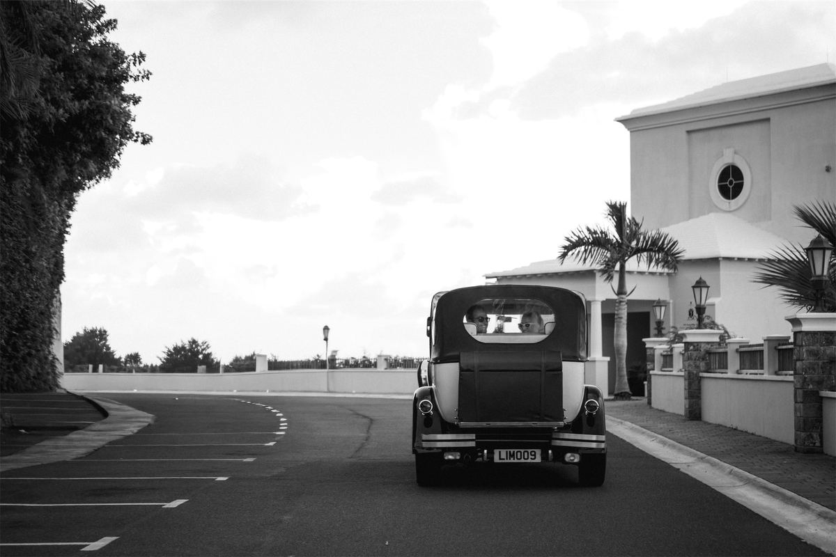 Black and white of a vintage car waiting on the road outside a white building