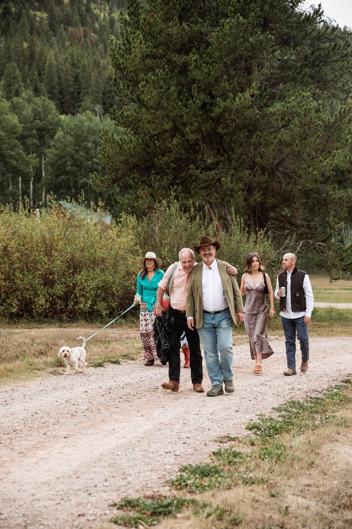 Family walks the dirt road with a small white dog to the welcome party at a mountain ranch among the aspens