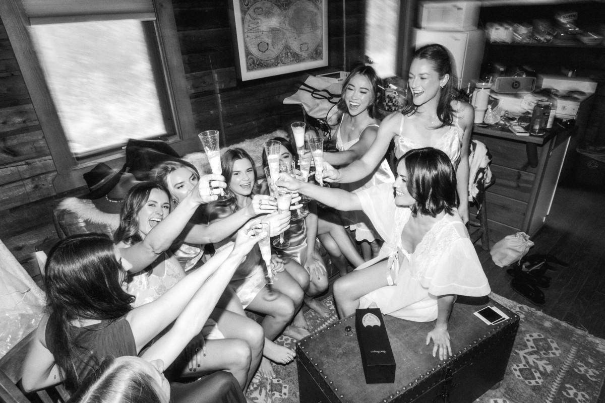 Devin and her bridesmaids toast with champagne in the cabin at a mountain ranch among the aspens, black and white