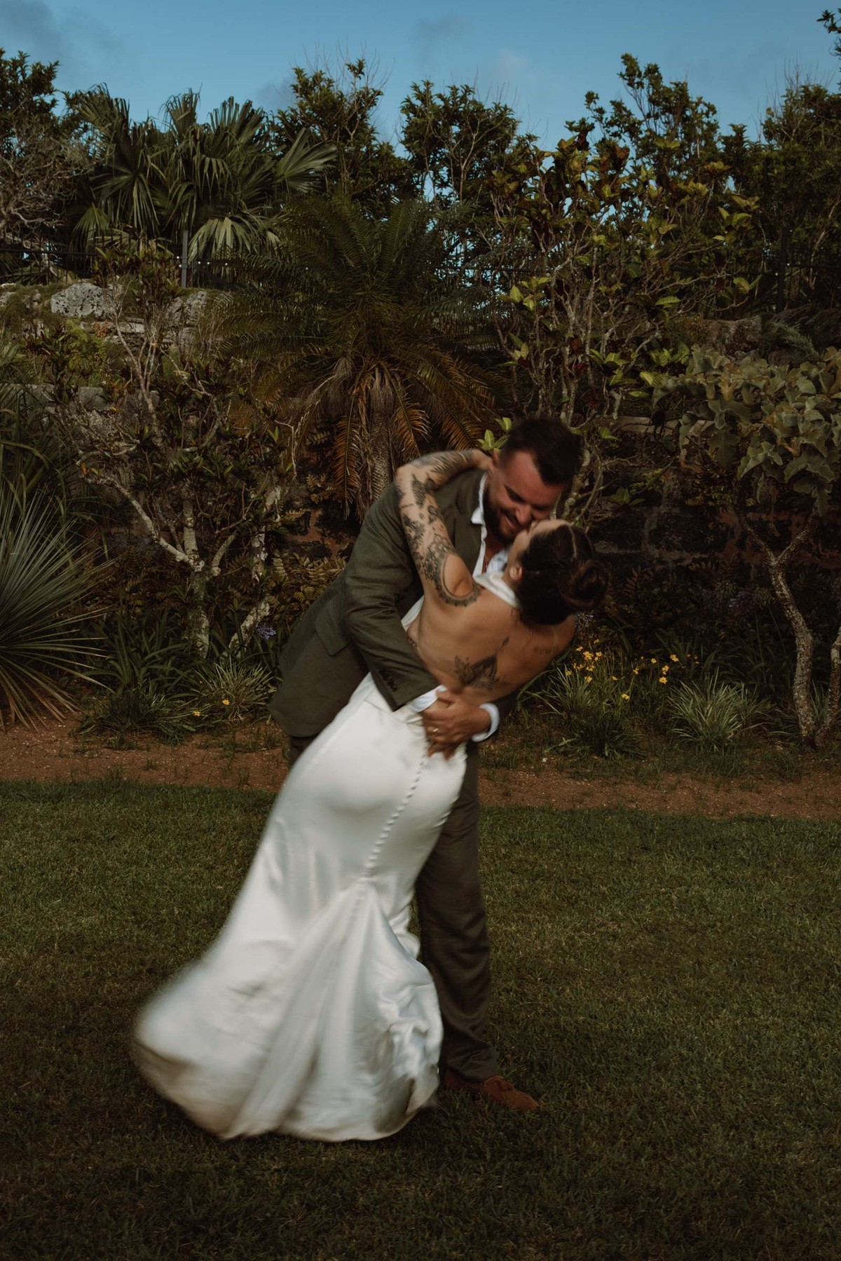 Groom dipping the bride for a kiss in front of a Bermuda stone wall