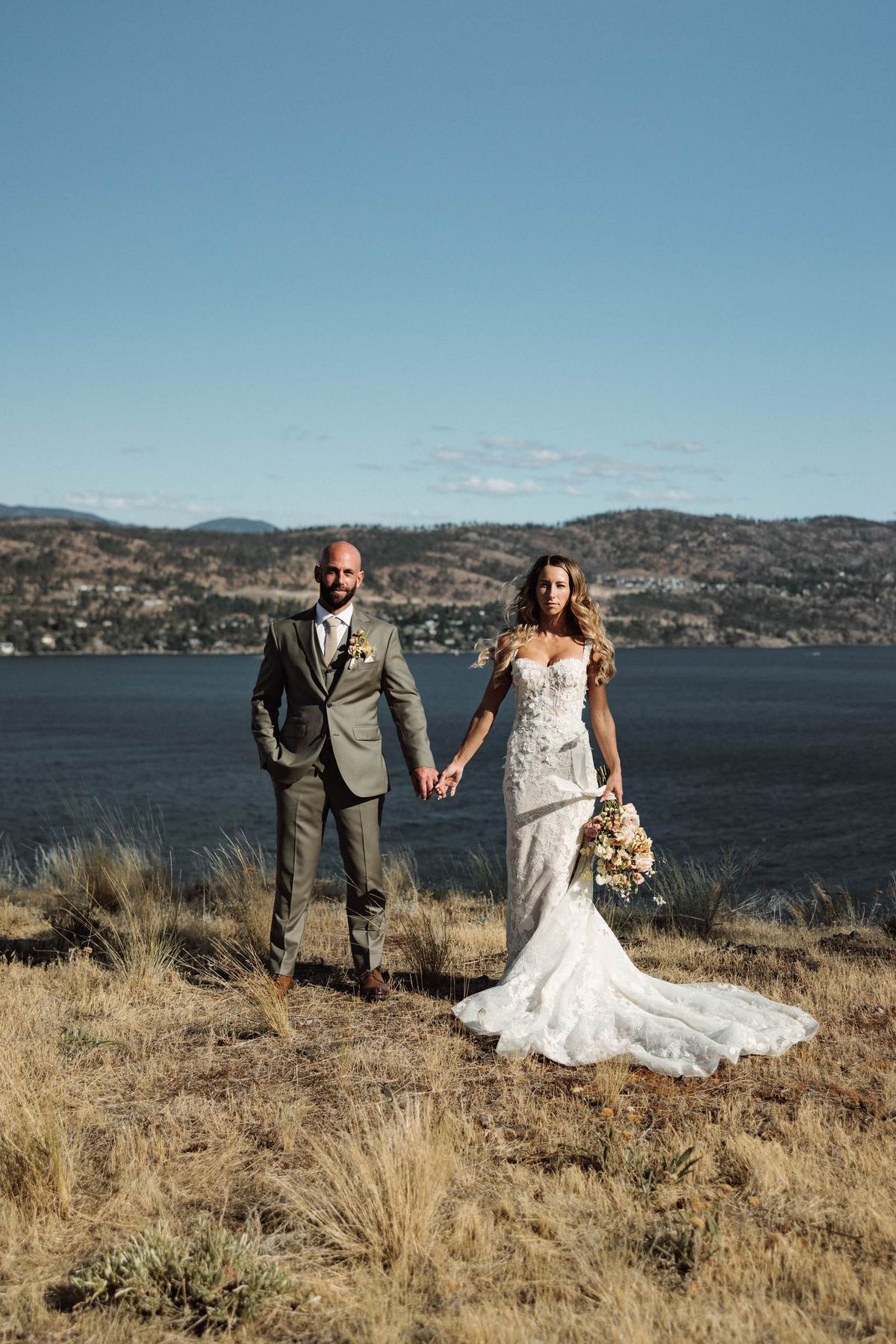 Bride and groom standing together on the hillside above the lake